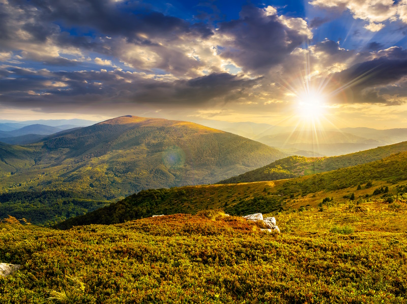 white sharp boulders on the grassy meadow on the edge of hillside in high mountain range in evening light