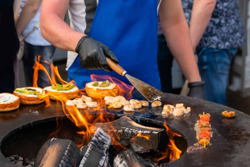 Chef preparing fish burgers with seafood, avocado, shrimp, prawn on brazier with hot flame at summer local food market - close up view. Outdoor cooking, gastronomy, cookery, street food concept
